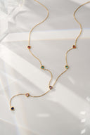 Gold tone lariat necklace with rainbow heart crystals laid on white