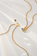 Gold tone birthstone charm necklaces with an open ring clasp and square crystal charms, laid flat
