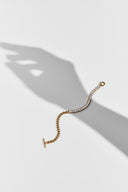 Gold tone baguette crystal tennis bracelet with heart chain and T-bar toggle on white with a hand shadow