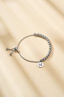Rose gold beaded bolo bracelet with engraved initial charm on marble surface — AURA Jewelry