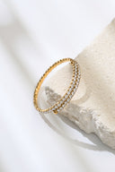 Gold tone double row crystal flex bangle leaning on a stone block