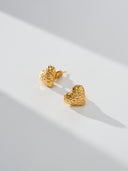 Textured heart stud earrings in gold and silver with a sculptural hammered finish, shown as minimalist heart earrings for women. Gold heart earrings and silver heart studs displayed as romantic gift jewelry, everyday stud earrings, and modern heart shaped earrings with a soft reflective surface.