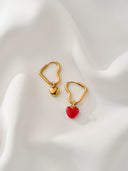 Gold heart hoop earrings with red enamel and gold heart charm on white fabric - AURA Jewelry