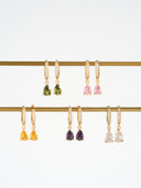 Gold birthstone huggie earrings with crystal huggie hoops and pear shaped gemstone drops arranged in several birth month color options. These dainty drop earrings are shown as elegant gift for her jewelry, birthday gift earrings, minimalist gold earrings, and personalized birth month earrings. Teardrop gemstone charm earrings with a refined everyday look, perfect for bridesmaid gifts, anniversary gifts, or stacking with other delicate jewelry pieces.

